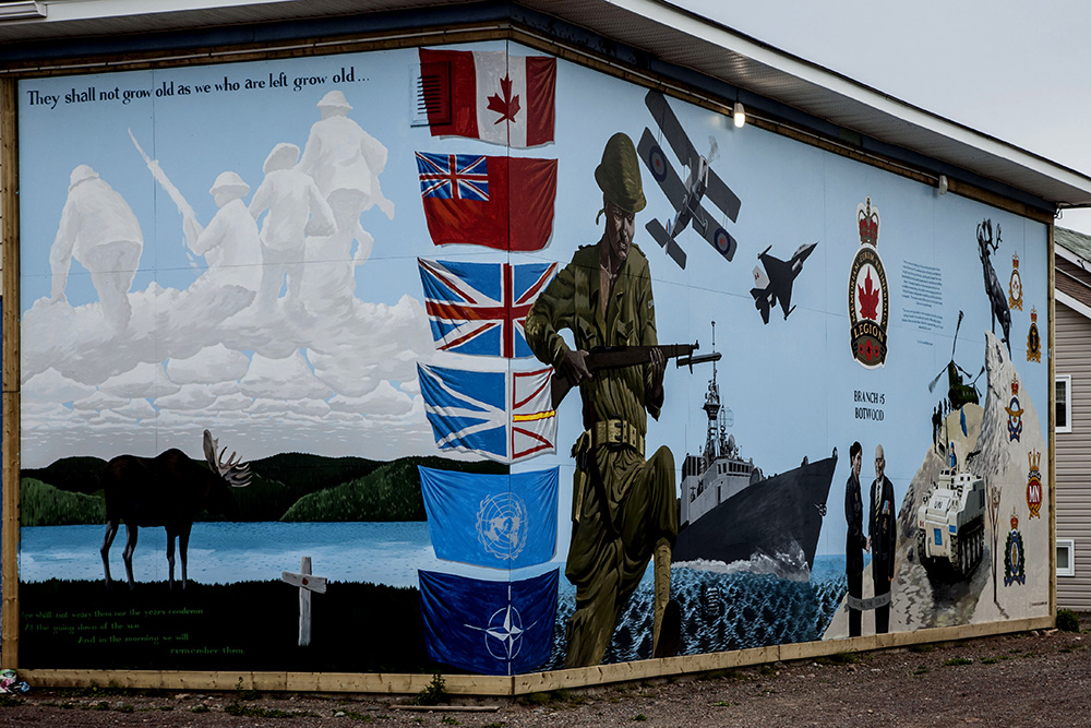 A wartime mural on the side of a building, featuring a soldier, airplanes, and a ship.