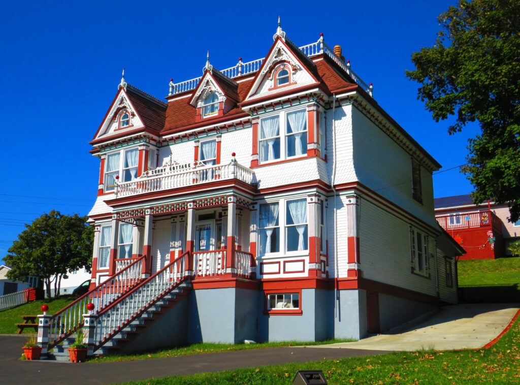 A colorful, Victorian style cottage sits upon a small hill.